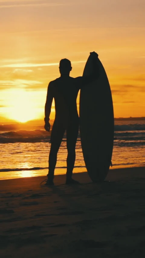 Silhouette of a fit guy standing on the beach with his surfboard at sunset Stock Footage 328362708