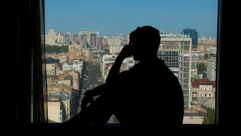 Silhouette of a frustrated guy sitting on a window in high floor Stock Footage 89324463