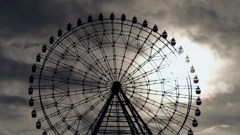 Silhouette of giant ferris wheel with cabins rotating against dramatic grey sky Stock Footage 246865053