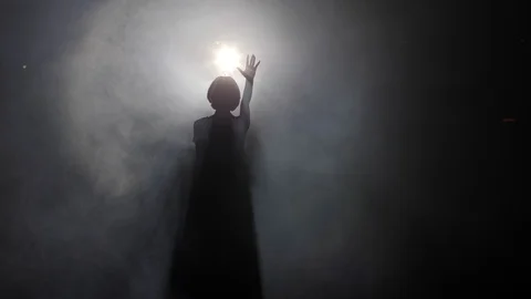Silhouette of girl with raised hand standing at bright light Stock Footage