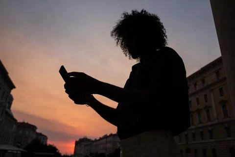 Silhouette of a guy with afro using his smartphone during sunset in the cit.. Foto stock