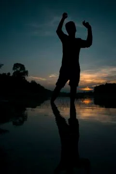 Silhouette of a guy posing in front of a beautiful sunset, reflecting on the Stock Photos