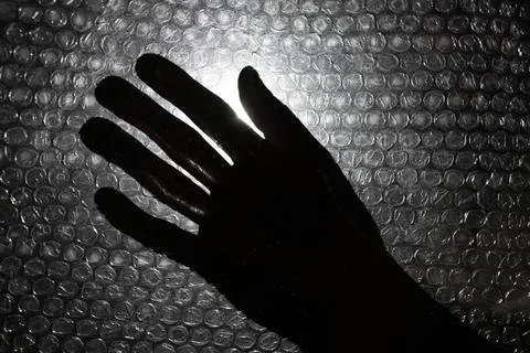 Silhouette of a hand seen through bubble wrap. A dark, emotional scene involv Stock Photos