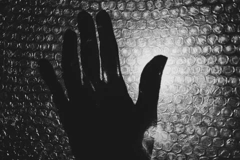 Silhouette of a hand seen through bubble wrap. A dark, emotional scene involv Stock Photos