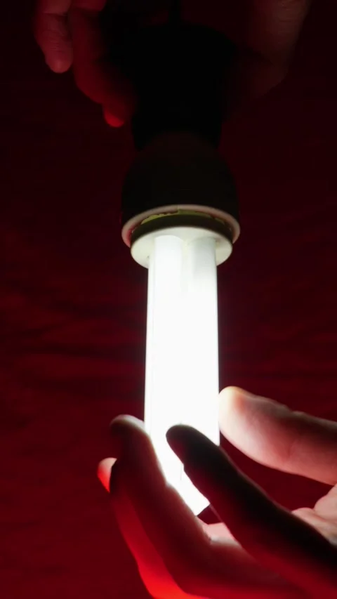 Silhouette of Hands Holding a Fluorescent Light Bulb in Dark Red Lighting Stock Footage 334136157
