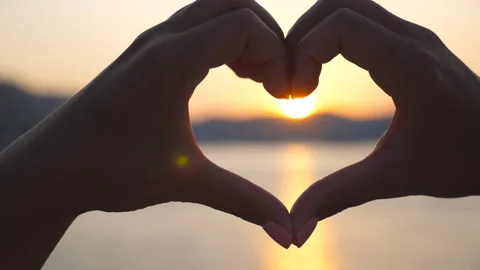 Silhouette of hands making heart shape over sea background with beautiful sunset Stock Footage 305705513