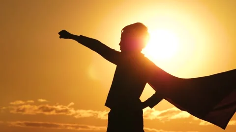 The silhouette of a kid during sunset raises his hand to the sun. Happy superher Stock Footage 243519049