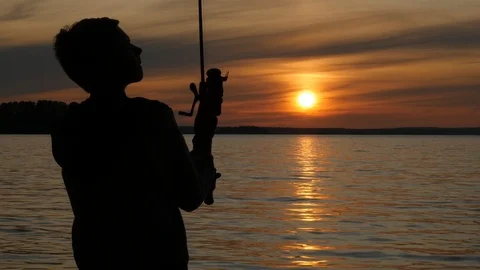 Silhouette of kid with rod fishing on beautiful lake during sunset Stock Footage