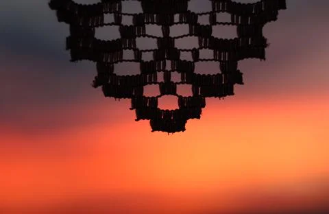 Silhouette of a knitted lace pattern against a vibrant orange sunset sky Stock Photos
