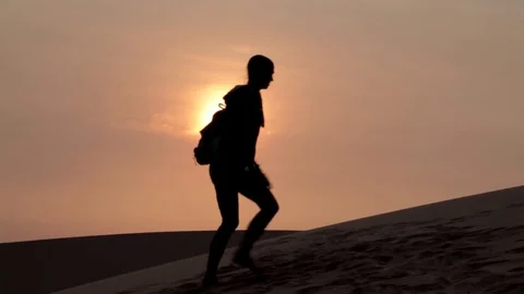 Silhouette of lonely woman going into desert, stops and drink water at sunset Stock Footage