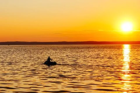 Silhouette a male fisherman in an inflatable boat floats on the Volga in suns Stock Photos