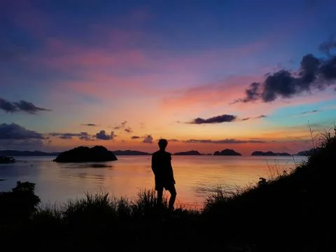 Silhouette of male standing on a hill looking at a colorful sunset in the Phi Stock Photos