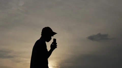 Silhouette of Man with cap talking on mobile phone while standing on field  Stock Footage 201646487