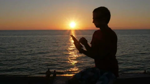 Silhouette man with digital tablet in hands at sunset beach. The sun is almost Stock Footage 67728260
