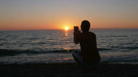 Silhouette man with digital tablet taking photo at sunset beach. The sun is Stock Footage 67728997