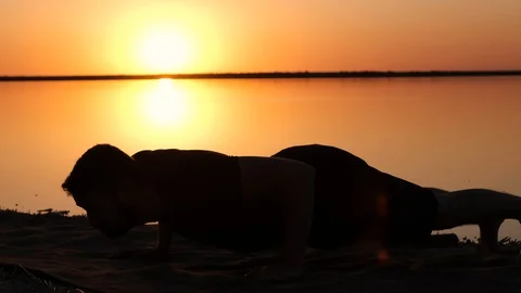 A silhouette of a man doing push ups on a seacoast against the sunset Stock Footage 91746768