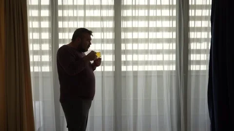 Silhouette of a man drinking herbal tea in glasses cup at the window Stock Footage 238525179