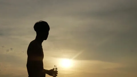 Silhouette of Man drinking water while resting on the field at sunset time.  Stock Footage 201643892