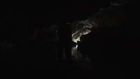 Silhouette of a man floating in a dark cave on a bamboo raft towards the exit. Stock Footage 99734340