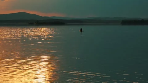 Silhouette of a man floating on a lake on a SUP board at sunset. Видео 337564226