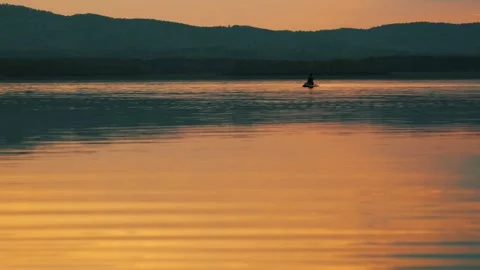 Silhouette of a man floating on a lake on a SUP board at sunset. Stockbeeldmateriaal 337564488