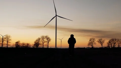 Silhouette of a man goes to sunset in the direction of wind turbines Stock Footage 104044236