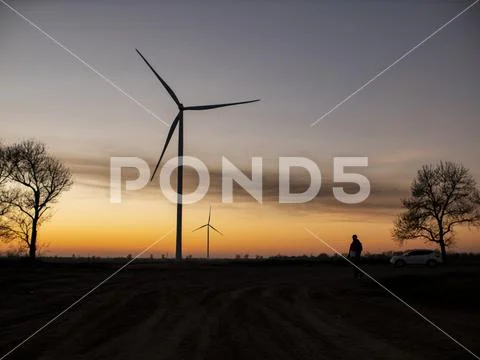 Silhouette of a man goes to sunset in the direction of wind turbines Stock Photos