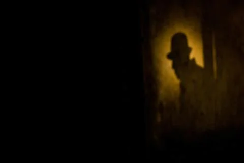 Silhouette of a man in a hat against a wall at night. Blur background with .. Stock Photos