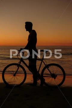 Silhouette of man on his bike on the beach Stock Photos