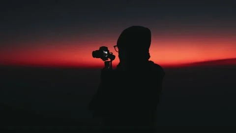 Silhouette of man holding camera at sunset 스톡 동영상 210554237