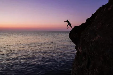 Silhouette of a man jumping from high cliffs into the sea Stock Photos