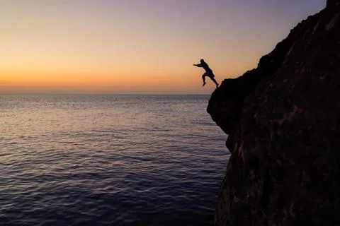 Silhouette of a man jumping from high cliffs into the sea Stock Photos