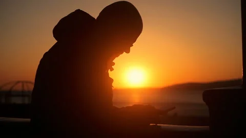 Silhouette of a man lighting a cigarette, the setting sun by the sea Vidéo 150227612