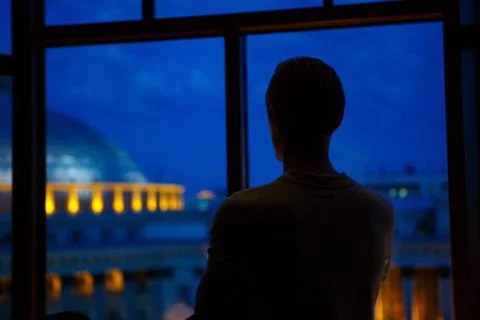 A silhouette of a man looking to the window on the evening cityscape Stock Photos
