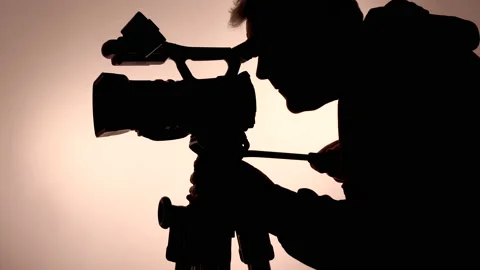 Silhouette of a man operating a video camera on a tripod. 스톡 동영상 146130128
