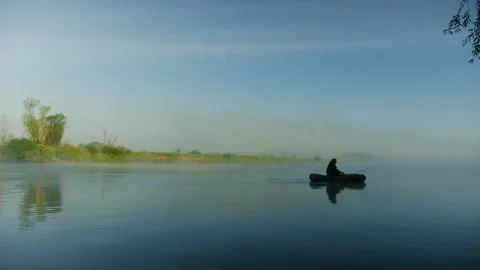 Silhouette of a man rowing in a boat while fishing on the lake.Foggy morning Stock Footage 238070447