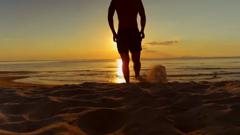 Silhouette Of Man Running Toward Ocean Across Sandy Beach During Golden Sunset L Stock Footage 331875713
