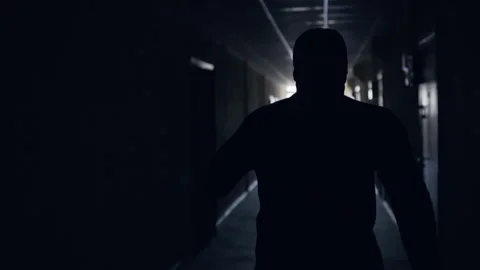 Silhouette of man runs down dark corridor to light at end and waves his arms Stock Footage 150211223