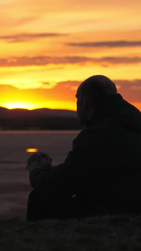 Silhouette of a man sitting alone on the shore of a lake at sunset. Stock-Footage 344021752