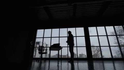 Silhouette of a man in a spacious office on the background of a large window. Video stock 107768620