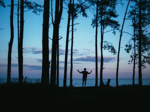 Silhouette man standing in forest rising hands with sea sunset background Stock Photos