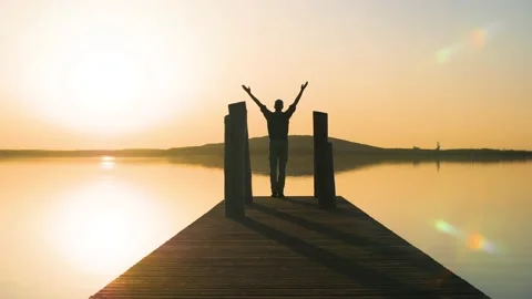 Silhouette of man standing on a pier doing yoga in nature at lake during sunset. Video stock 151395099