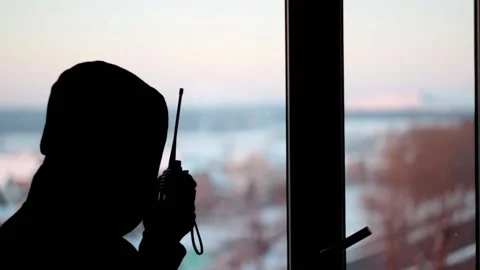 Silhouette of a man stands in front of the window speaks into a walkie-talkie Stock Footage 146775773