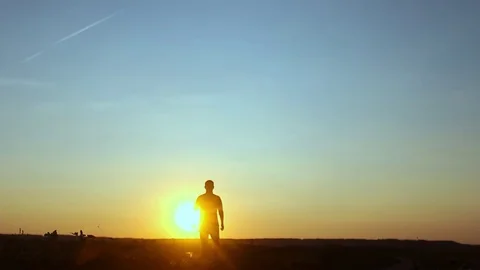 Silhouette of man at sunset. The man goes to the far side, the lower angle. Trav Stock Footage