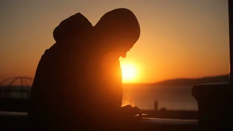 The silhouette of a Man at sunset writes a message to a smartphone 库存影片 150227337