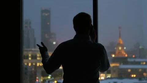 Silhouette of a man talking on the phone by the window view of the night city Video stock 135429261