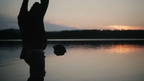 Silhouette man throwing large stone at lake sunset Stock Footage 77965999