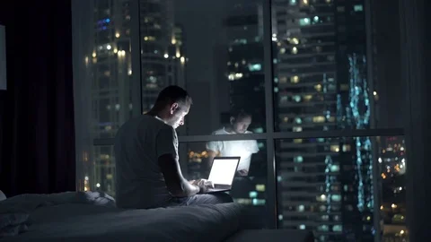 Silhouette of man using laptop and falling asleep on bed at night at home, 4K Stock Footage 70340885