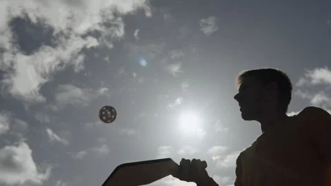 Silhouette of man using racket to hit spinning pickleball ball against sky. Stock Footage 254757201