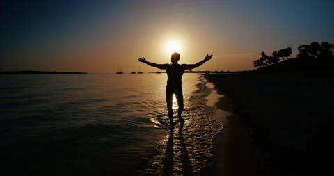 Silhouette of Man Walking Along Beach at Sunset with Feet in Waves Stock Footage 343594851